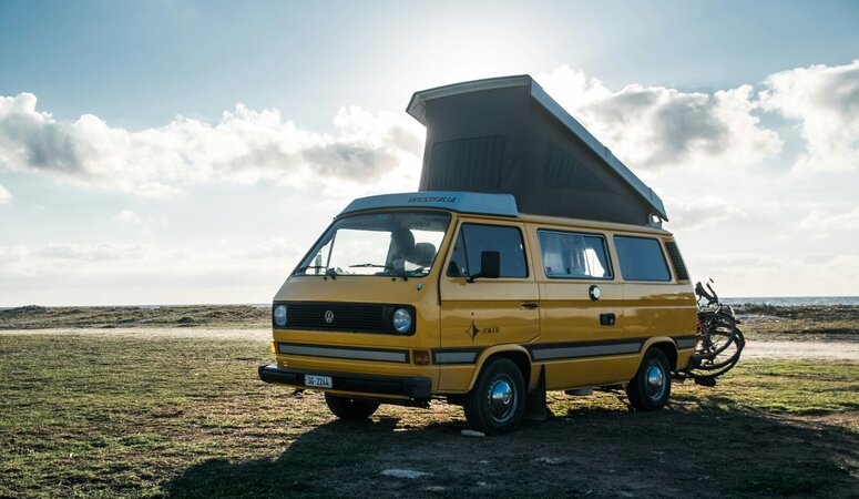 Gelbes VW-Bus-Wohnmobil mit Hochdach und zwei an der Heckklappe montierten E-Bikes.